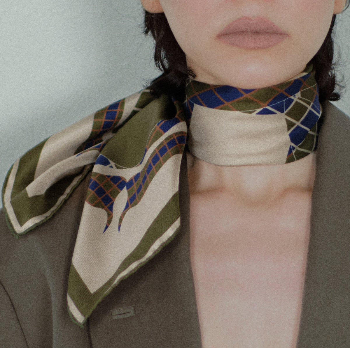 The Crossing silk carré worn knotted at the neck, the ends falling over the lapel of a jacket