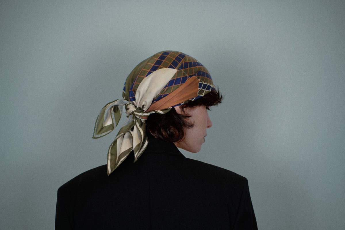 The Crossing silk carré tied over the hair, seen from behind — the knot and the hand-rolled edges