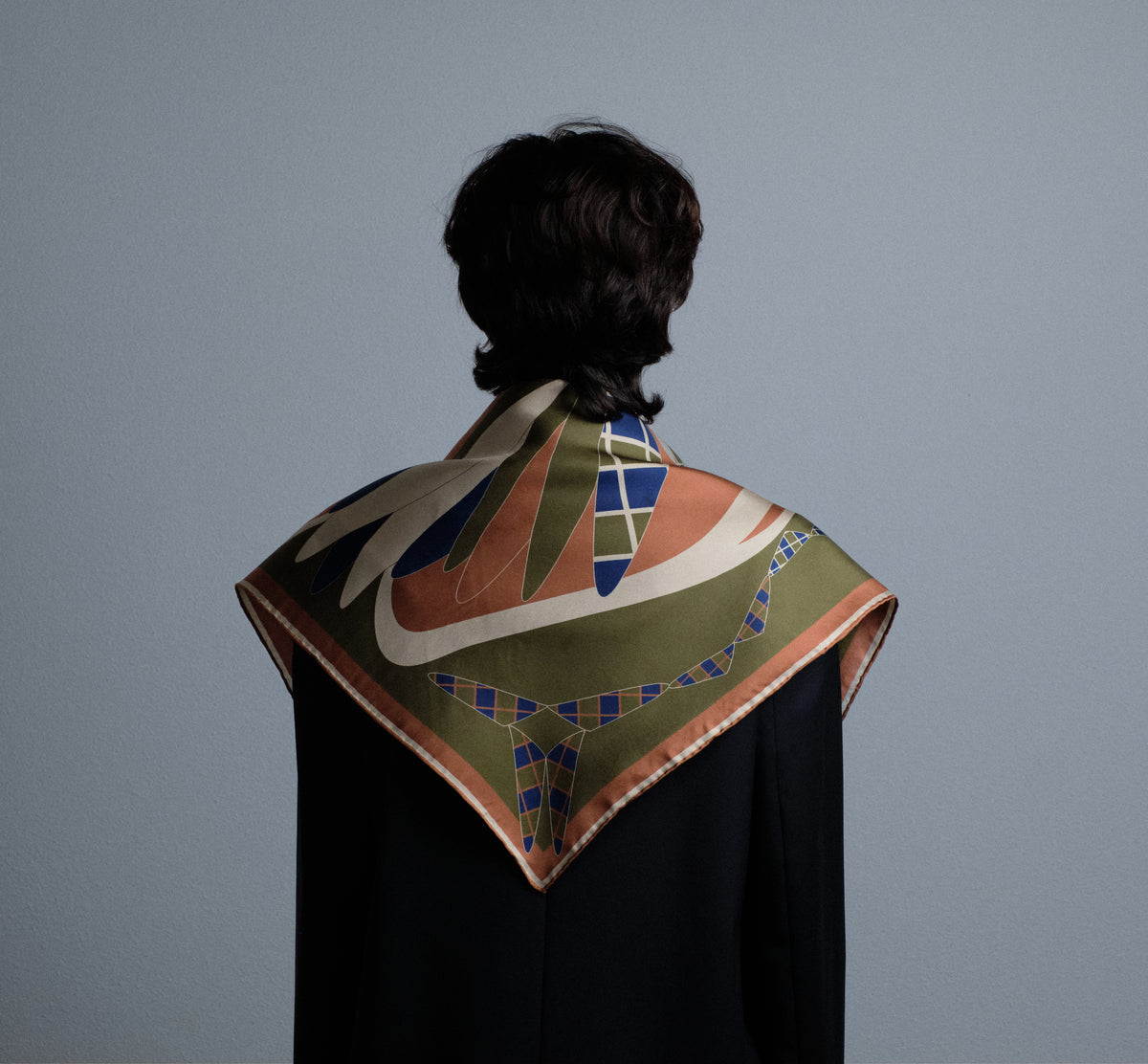 The Graft silk carré worn over the shoulders, seen from behind — the carob border and hand-rolled edges