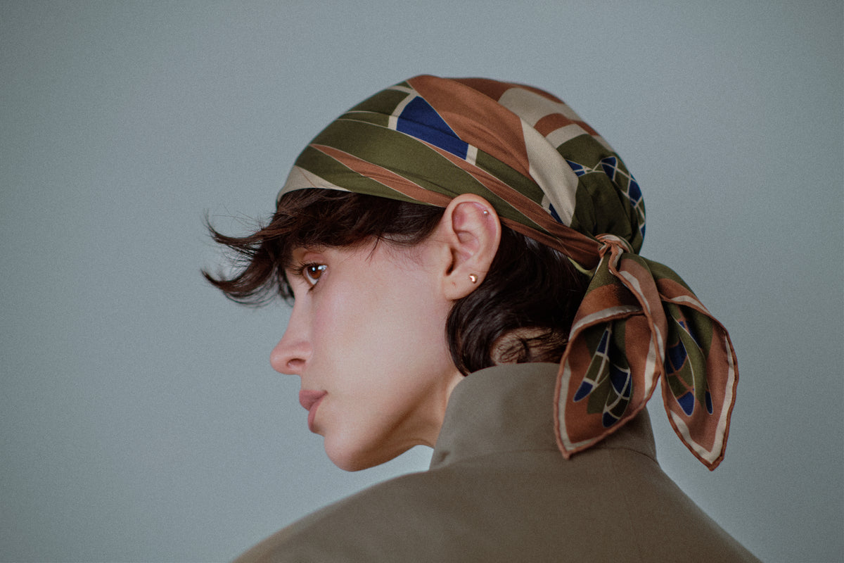 The Graft silk carré worn as a headscarf, seen in profile — the knot and the hand-rolled edges