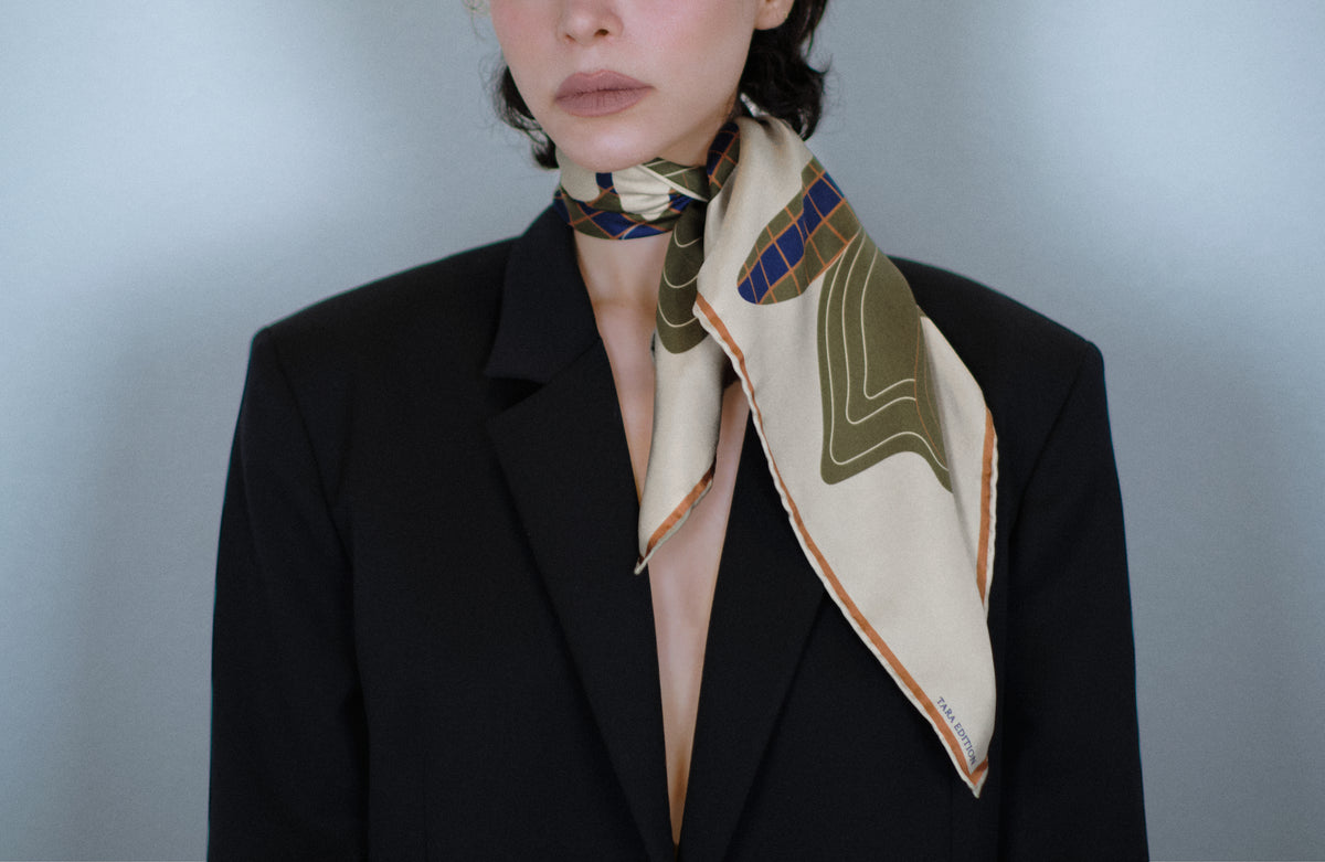The Quatrefoil silk carré knotted close at the neck, the signed corner falling over a dark jacket