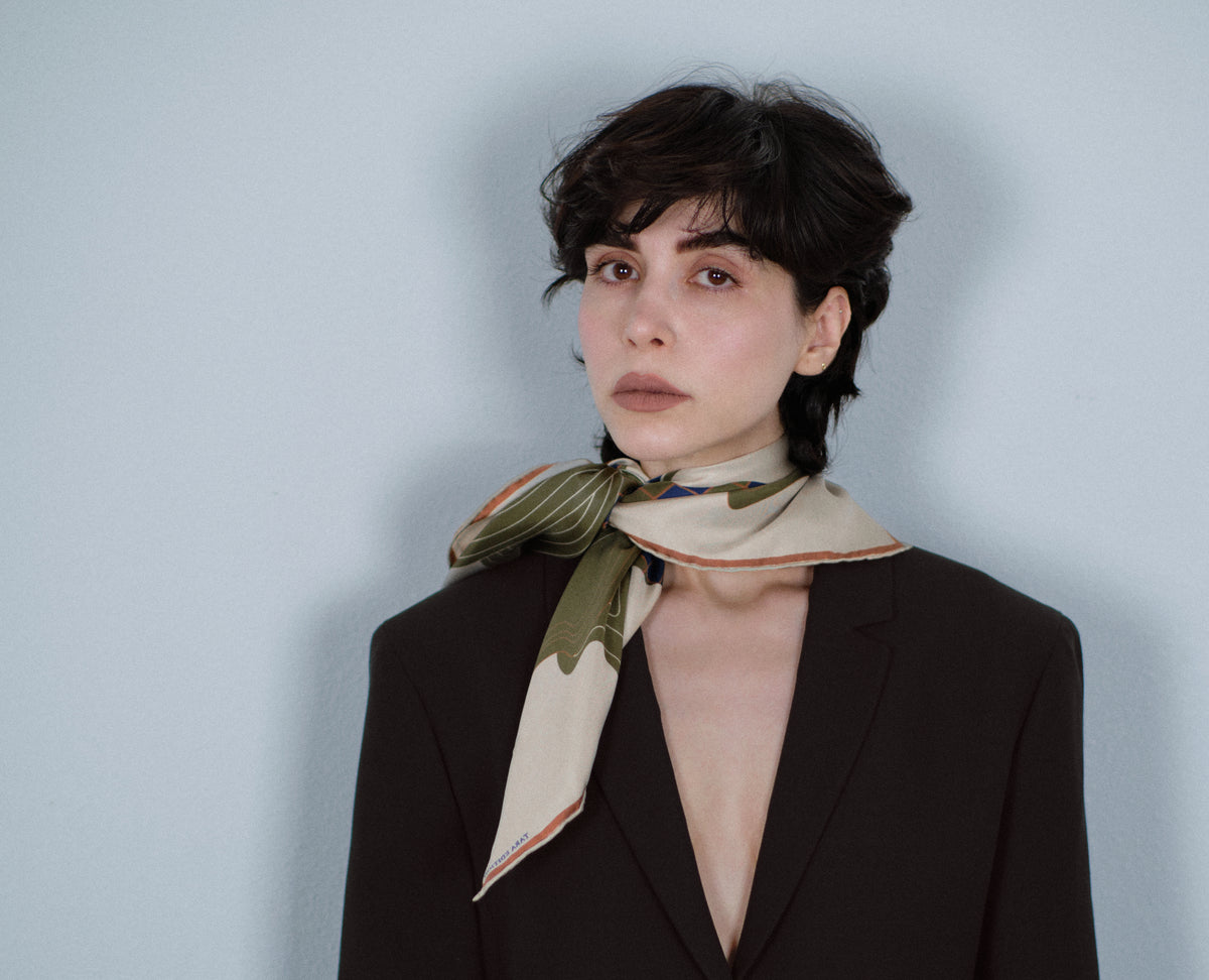 The Quatrefoil silk carré knotted loosely at the neck, over a dark jacket